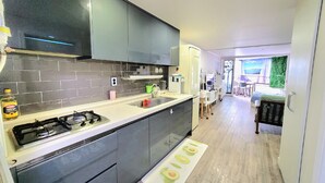 Una cocina moderna con armarios oscuros, encimera blanca y estufa a gas. Se observa, al fondo, un comedor con mesa y sillas.