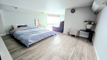 A bedroom with a bed, a small table, a chair, a clock, and a wall-mounted air conditioner.