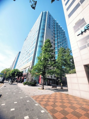 A modern high-rise building with a glass facade, surrounded by a pedestrian area with trees and benches. - Like U (Goyang)