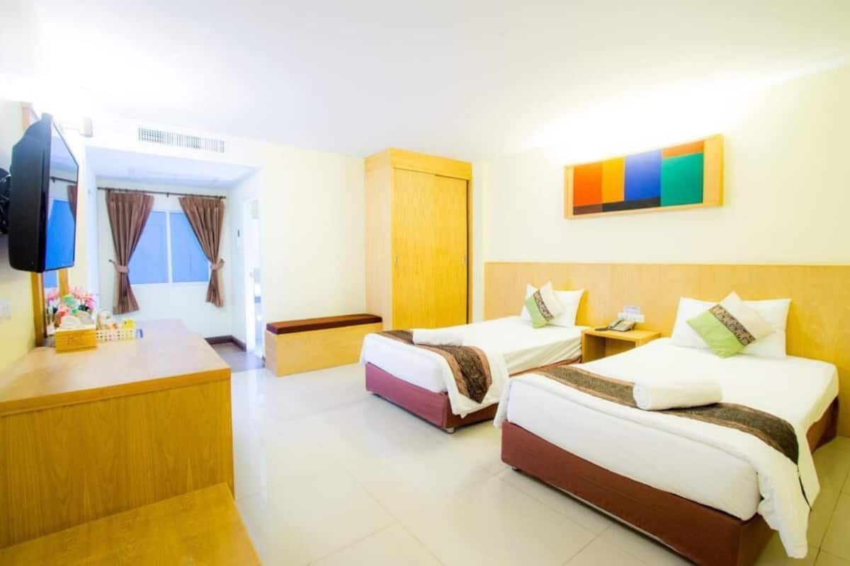 A hotel room with two beds, a desk, a television, and a window with curtains.