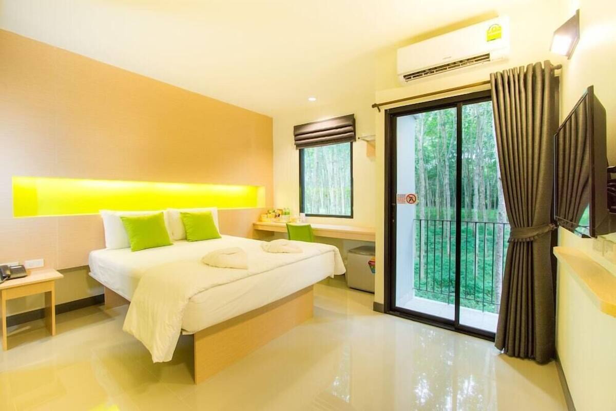 A modern hotel room with a bed, bedside table, and a view of a balcony with greenery.