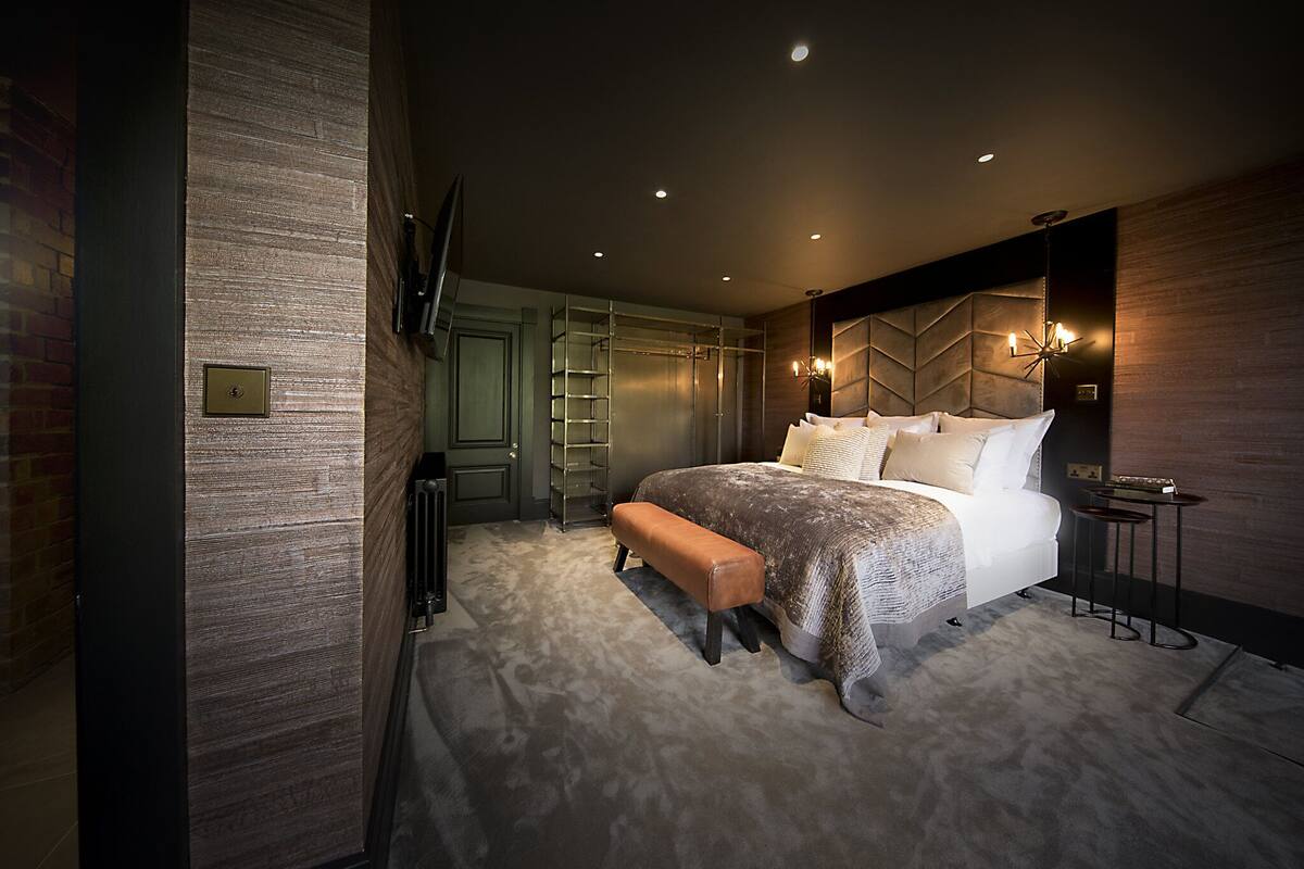 A modern bedroom with a large bed, a bench, a TV mounted on the wall, and a built-in shelving unit.