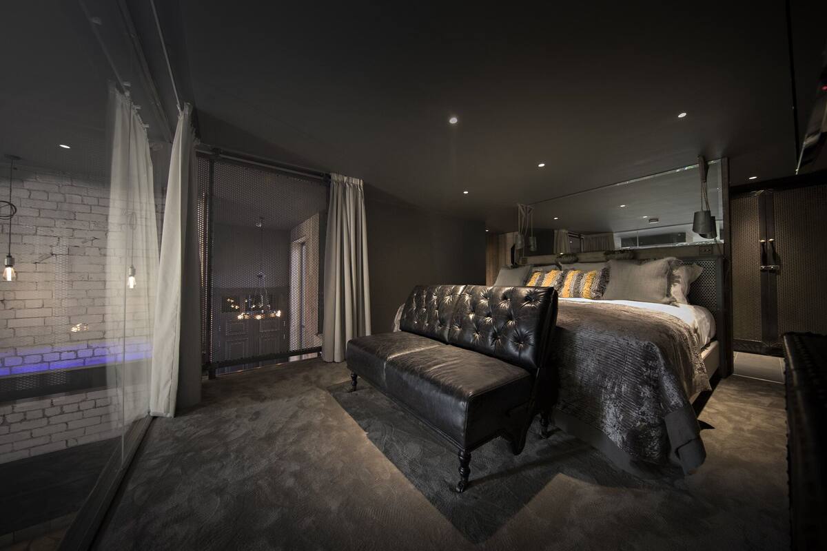 A modern bedroom with a large bed, a bench, and a view of the city through large windows.