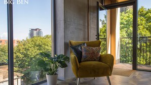 A modern room with a large window, a yellow armchair, a potted plant, and a herringbone wooden floor. - The Bells (Leeds)