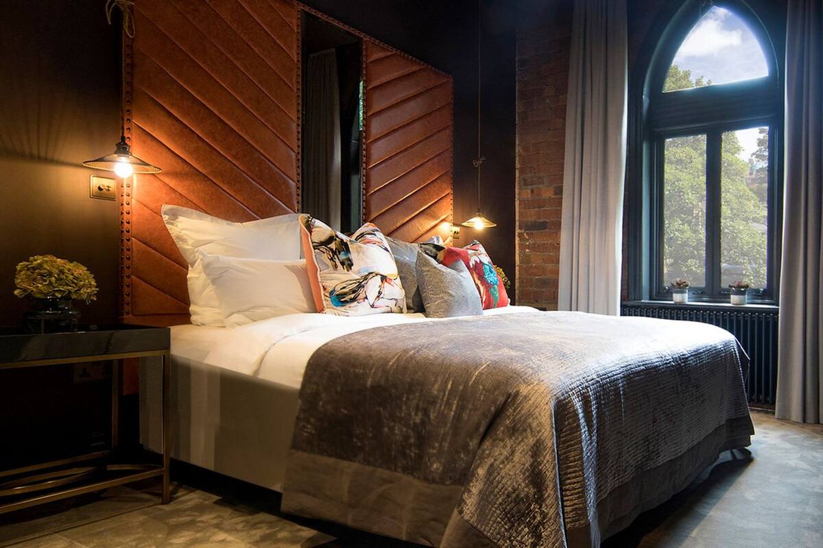 A bedroom with a large bed, a wooden headboard, a window with curtains, and a nightstand with a lamp.