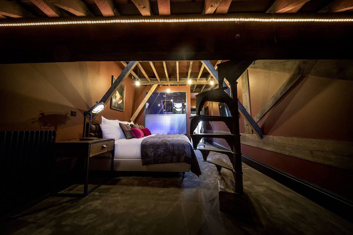 A cozy attic bedroom with a bed, a desk, and a ladder.