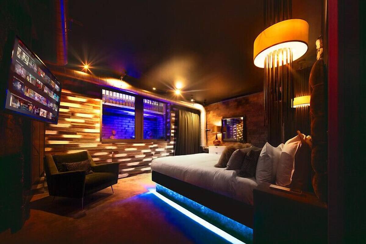 A modern bedroom with a large bed, a TV mounted on the wall, and a unique lighting fixture.