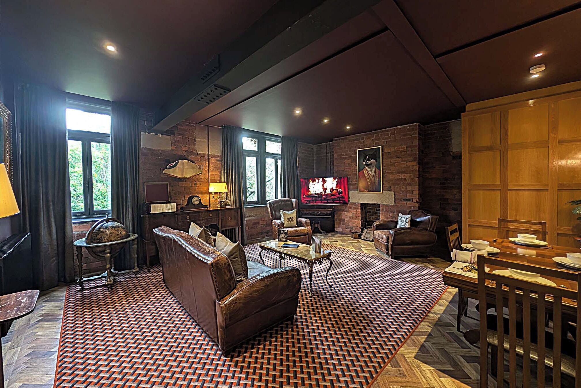 A spacious living room with a fireplace, leather sofas, a dining area, and a large TV screen.