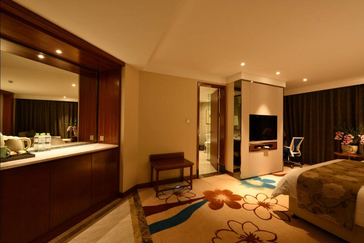A hotel room with a bed, a desk with a chair, a TV, and a bathroom visible through an open door.