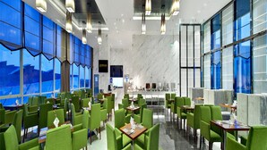 Een modern restaurant met groene beklede stoelen, marmeren vloeren en grote ramen met uitzicht.