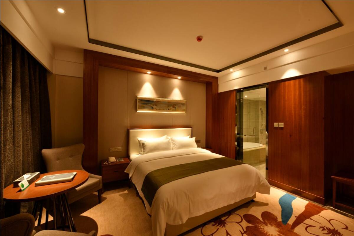 A hotel room with a bed, a desk, a chair, a small table, and a shower area.