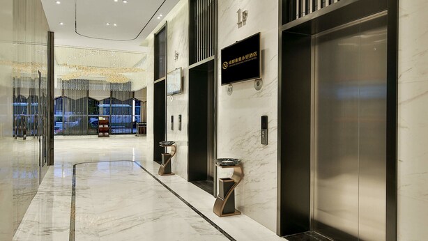 Een moderne hotellobby met marmeren vloeren, liften en een glazen wand.