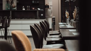 A modern dining area with a long table and chairs, a kitchen in the background, and a hanging light fixture. - 3G Hotel (Fulda)