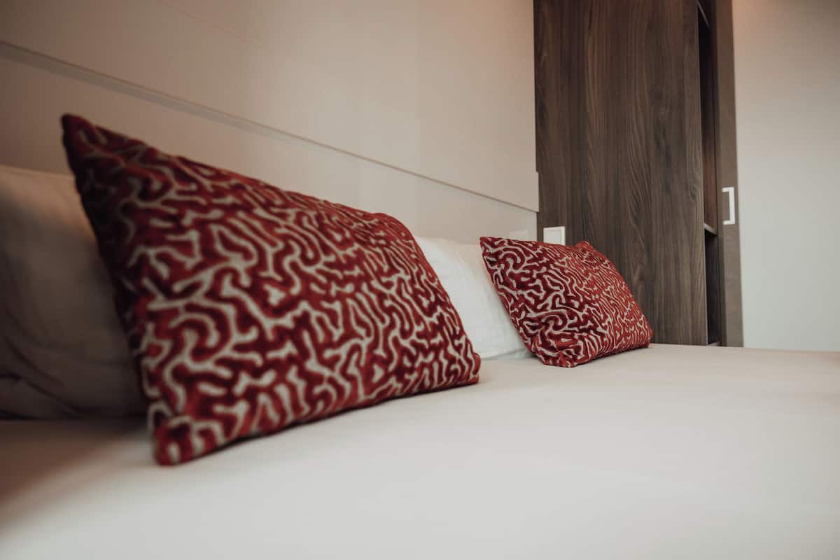 A bed with two pillows, a wooden door, and a white wall.
