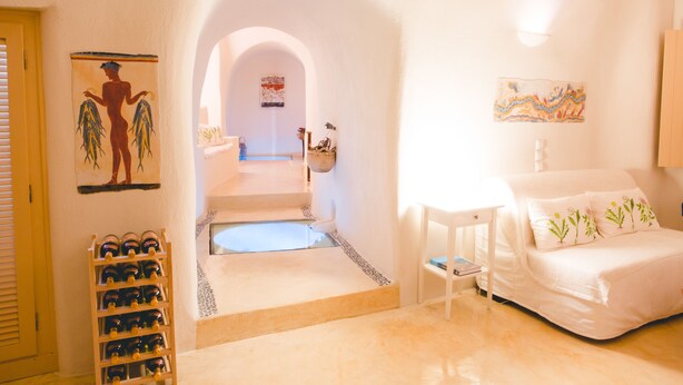 A hotel room with a bed, a small table, and a chair. There is a staircase leading to another room. - Flora's House (Santorini)
