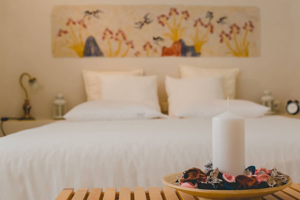 Un lit avec du linge de lit blanc et un mur blanc orné d’un tableau représentant des fleurs.