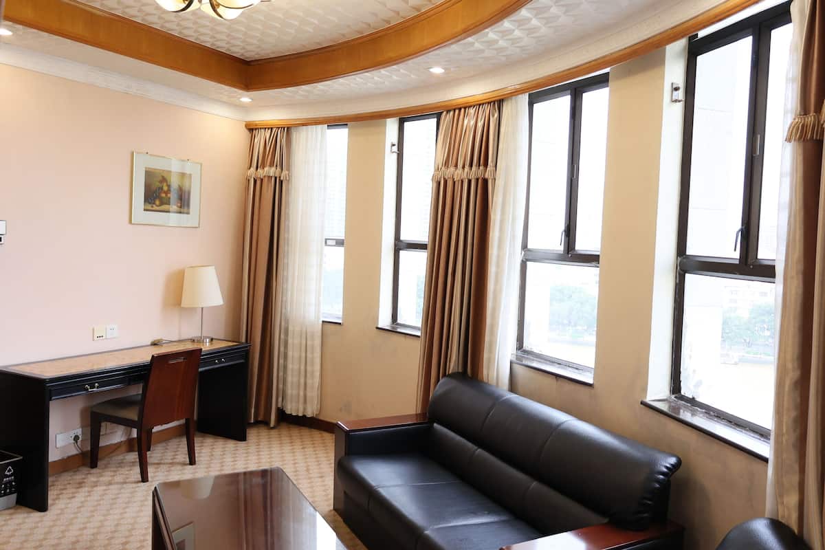 A hotel room with a desk, chair, sofa, and large windows with curtains.