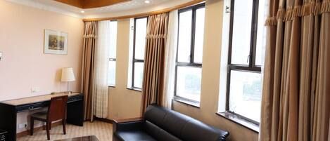 Une chambre d’hôtel équipée d’un bureau, d’une chaise, d’un canapé et de grandes fenêtres avec des rideaux.