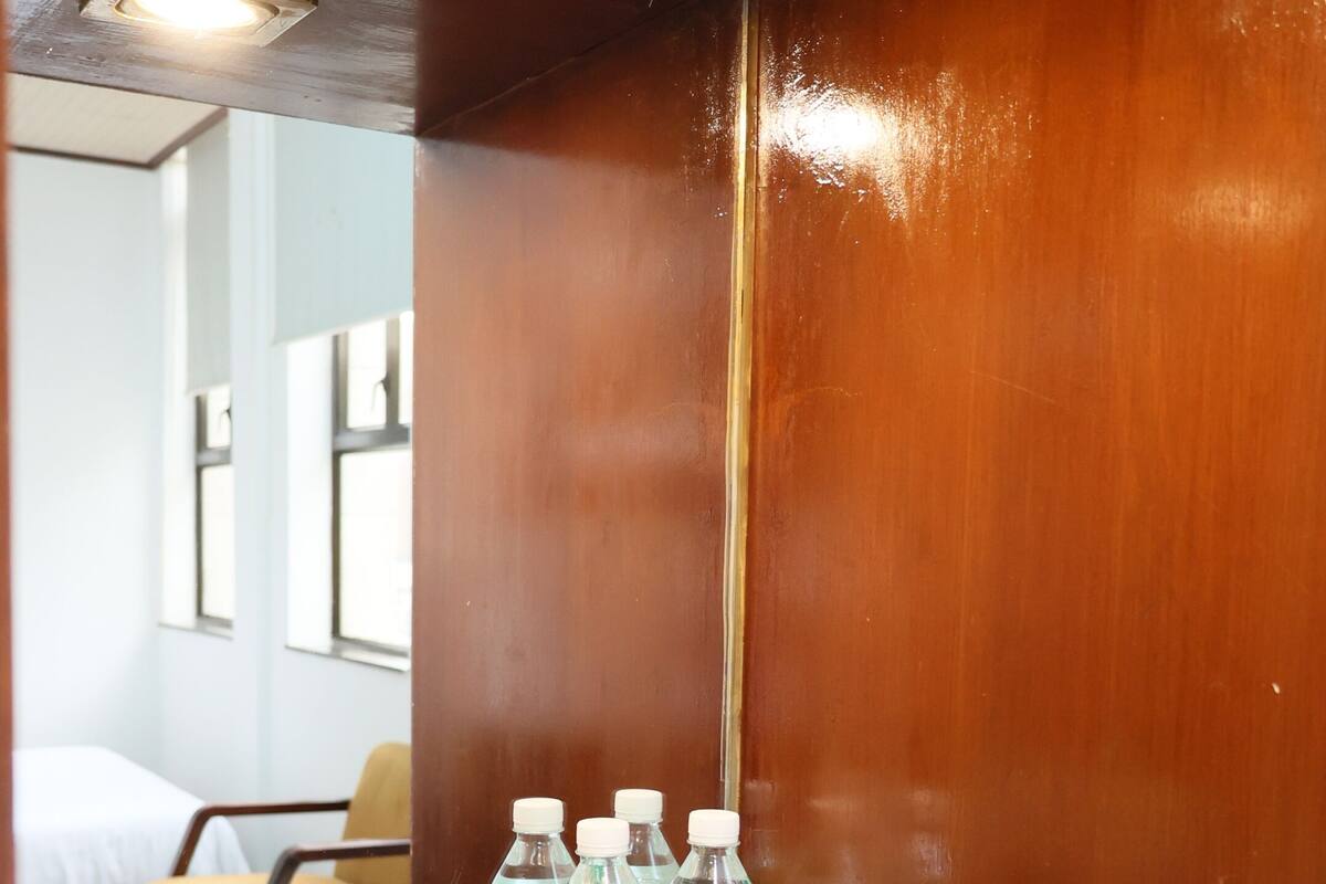 A hotel room with a wooden wall, a table with water bottles, a kettle, and a cup.