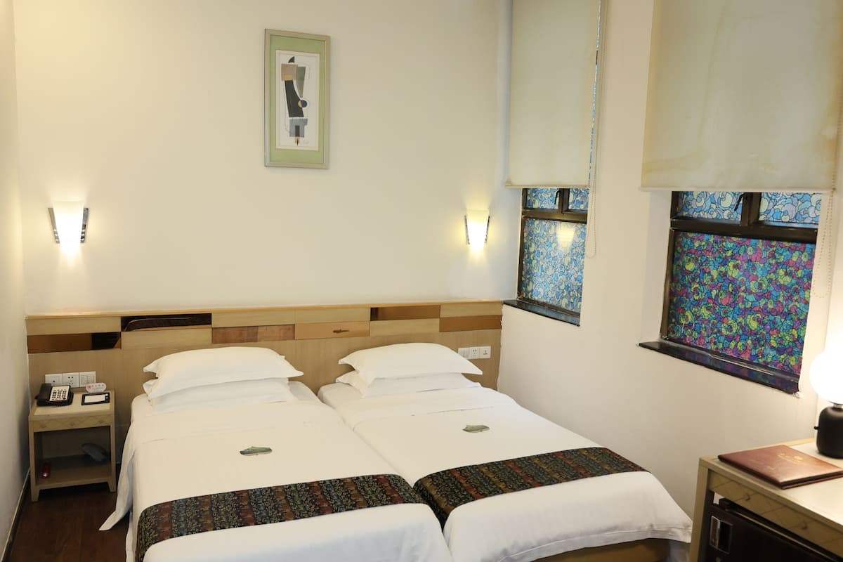 A double bed with a headboard, bedside tables, a small desk with a lamp, and a window with patterned curtains.