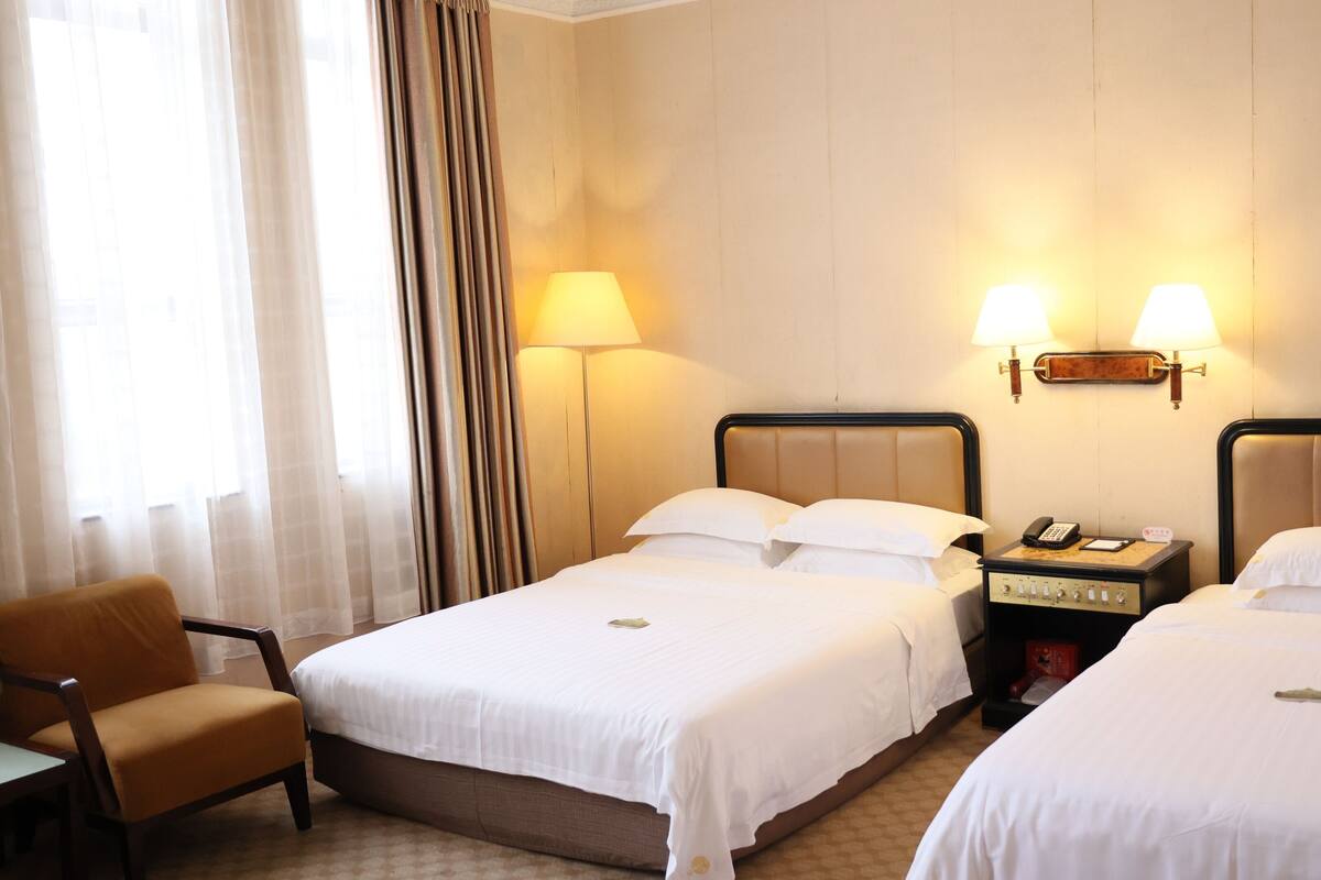A hotel room with two beds, a chair, a bedside table with a phone, and lamps.