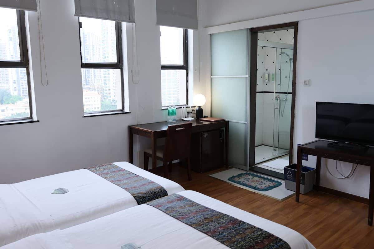 A hotel room with two beds, a desk with a computer, a TV, and a glass-enclosed shower area.
