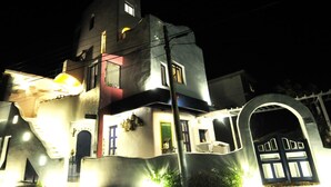 Un edificio de varios pisos con un diseño arquitectónico singular, que presenta una torre destacada, varias puertas y una entrada bien iluminada.