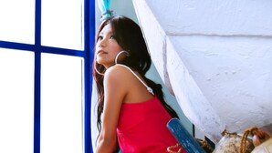 Una habitación con un ventanal grande, un barco blanco y una persona vestida de rojo sentada en el suelo.