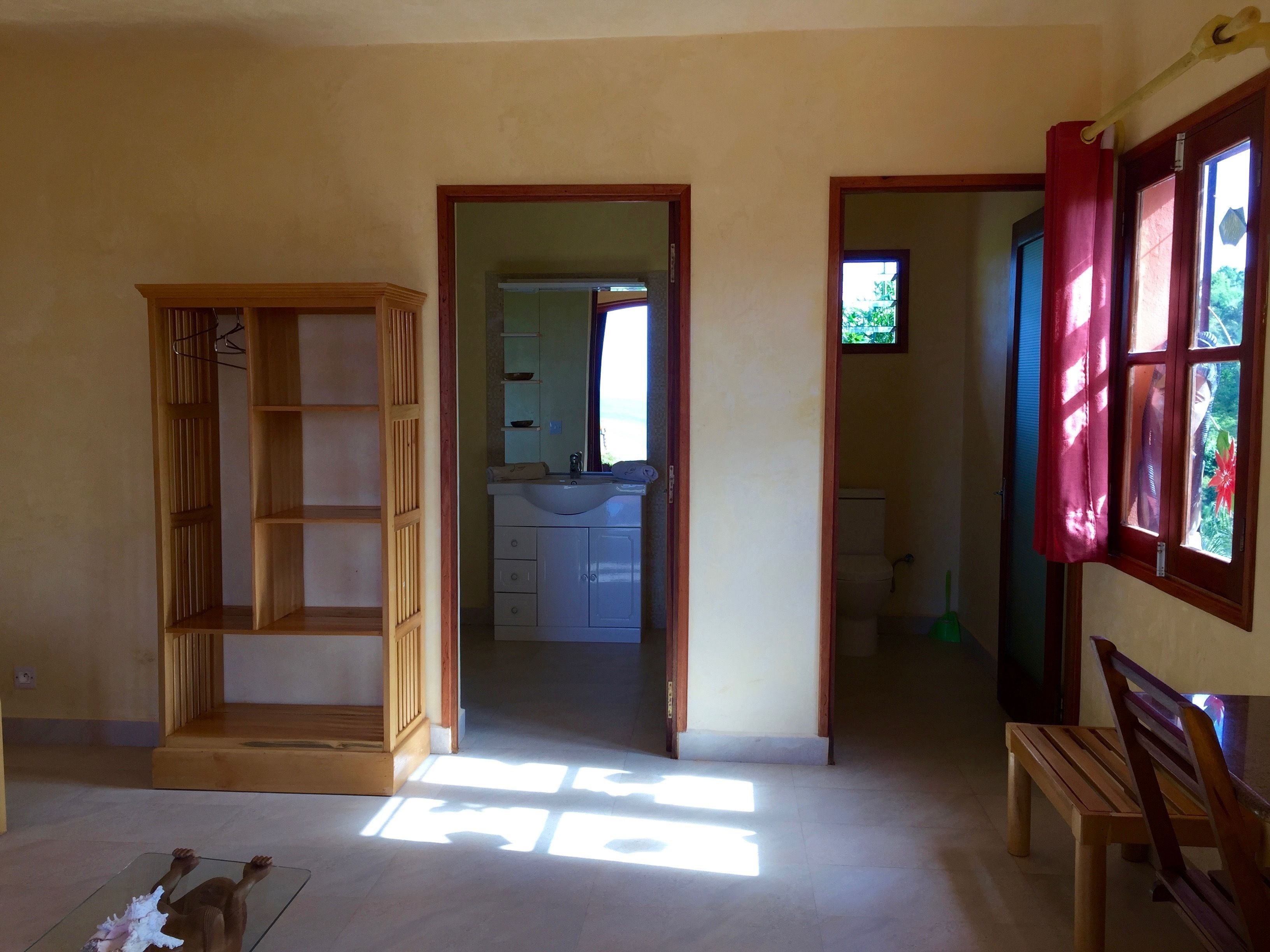 Une pièce avec une armoire en bois, un banc et une vue sur une salle de bain par une porte ouverte.
