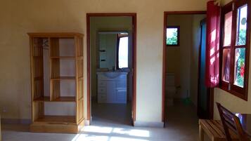 Une pièce avec une armoire en bois, un banc et une vue sur une salle de bain par une porte ouverte.