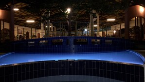 A swimming pool with a blue tiled edge, surrounded by a covered area with a high ceiling and structural beams. - Oasis Lodge (Fenoarivo Atsinanana)