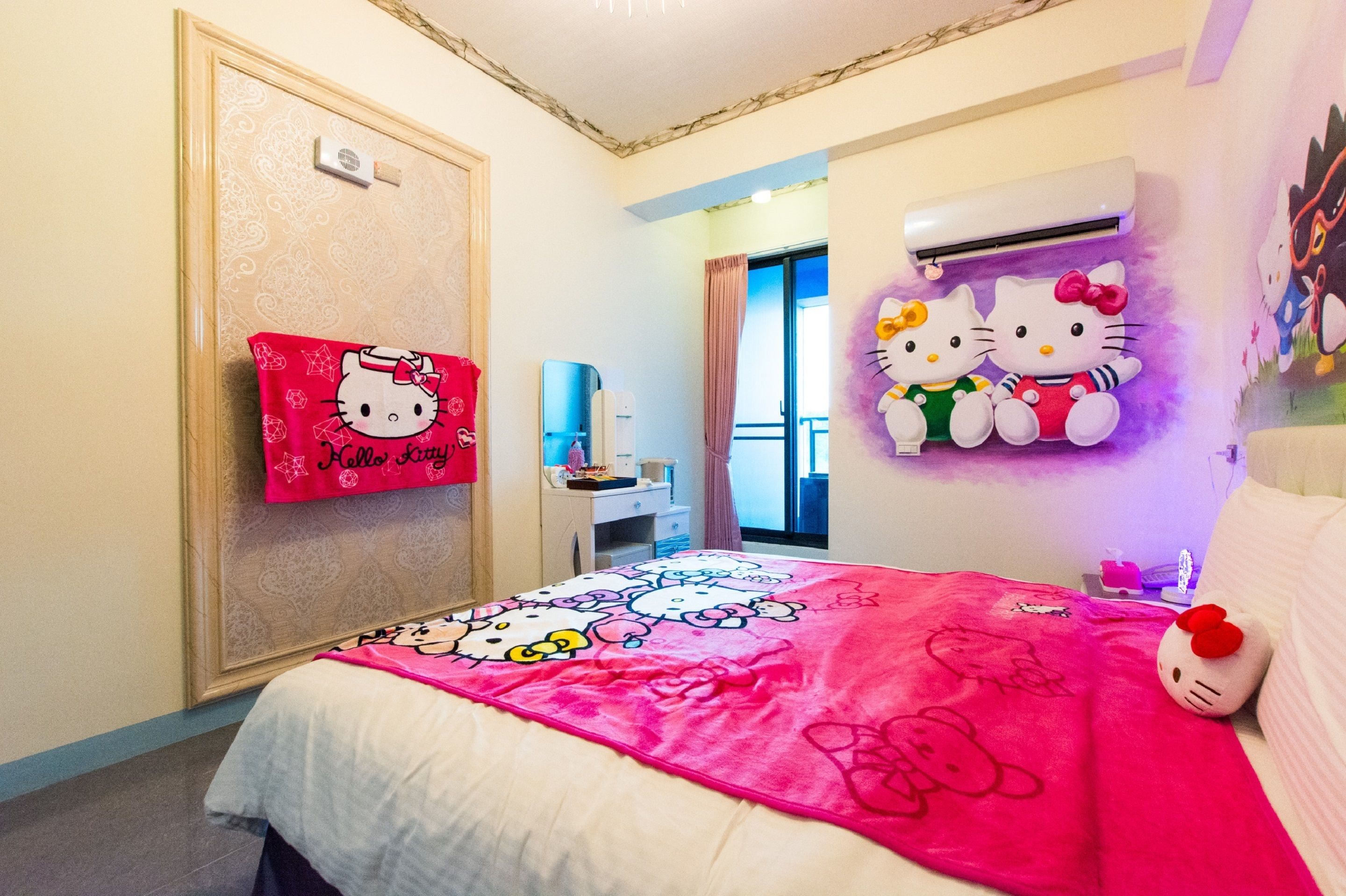 A hotel room with a Hello Kitty themed bedspread, a Hello Kitty pillow, and a Hello Kitty wall decoration.