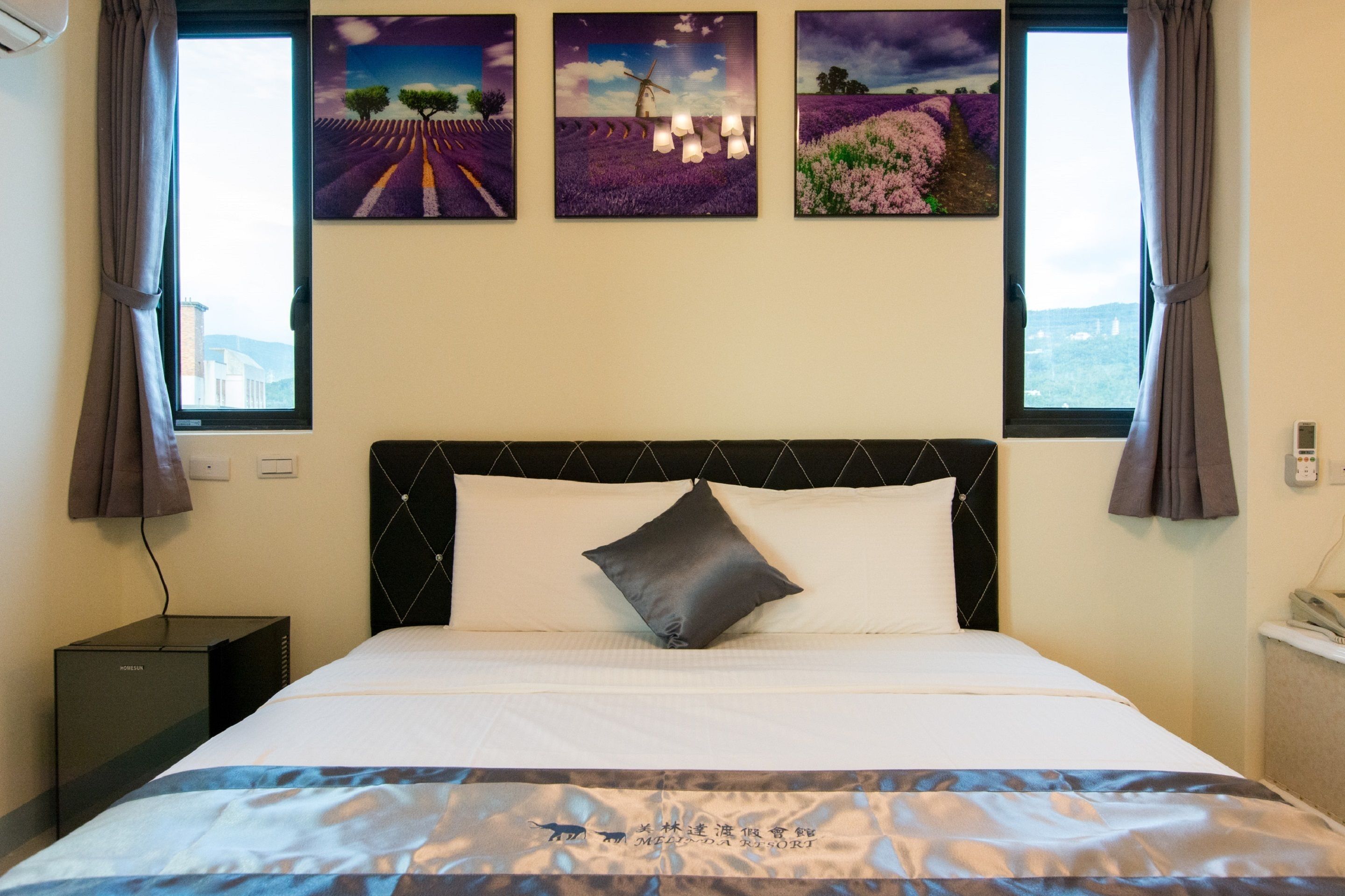 A hotel room with a bed, a nightstand, and a window with curtains.
