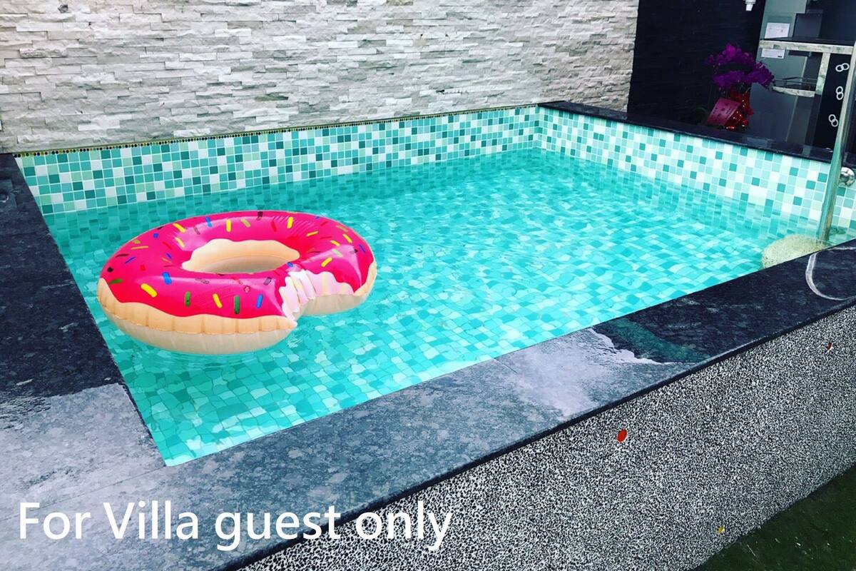 Una piscina con un flotador en forma de dona rosa, con azulejos en un patrón azul claro y un muro de piedra al fondo.