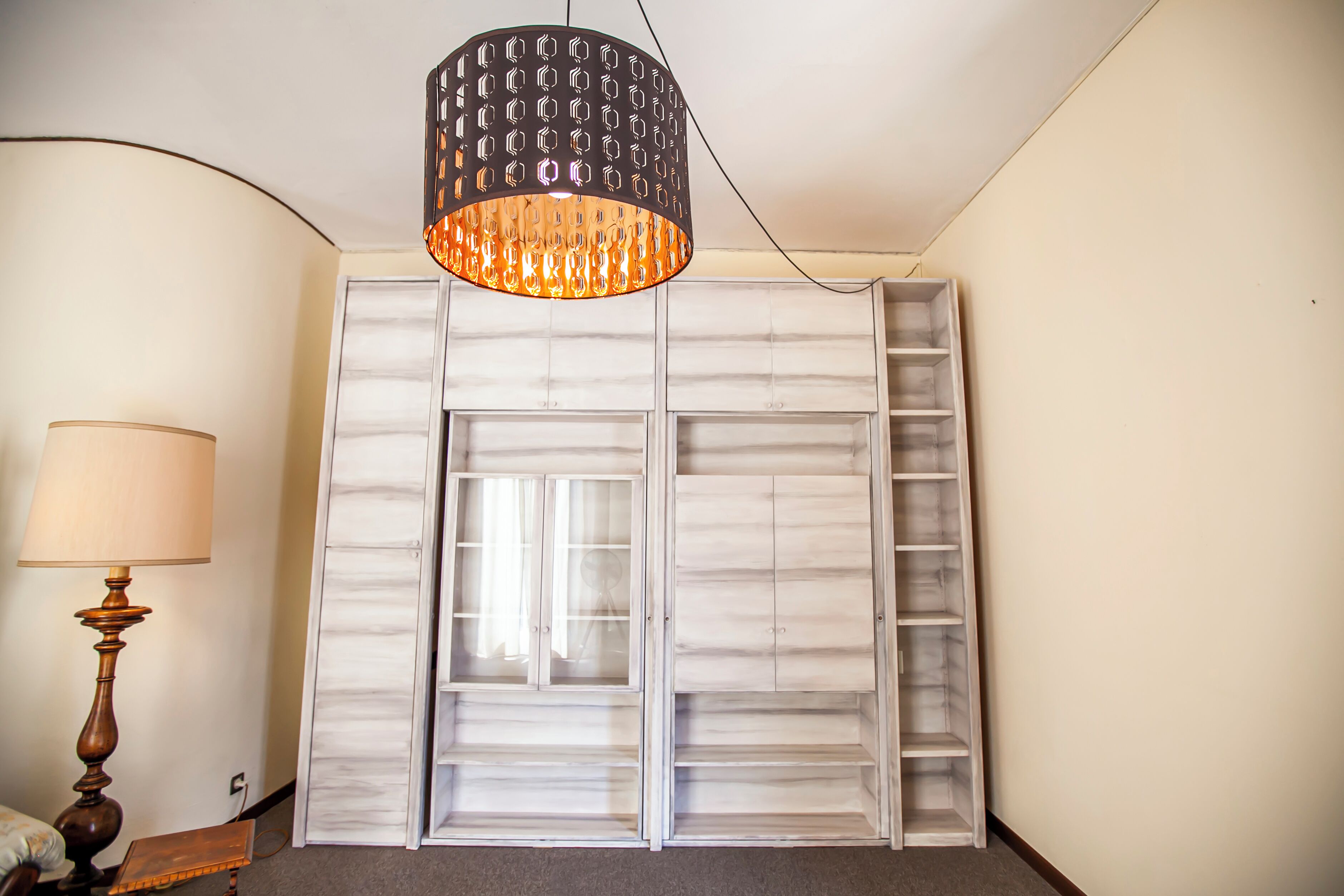 Ein Zimmer mit großem Kleiderschrank, einer Pendelleuchte und einer Stehlampe.