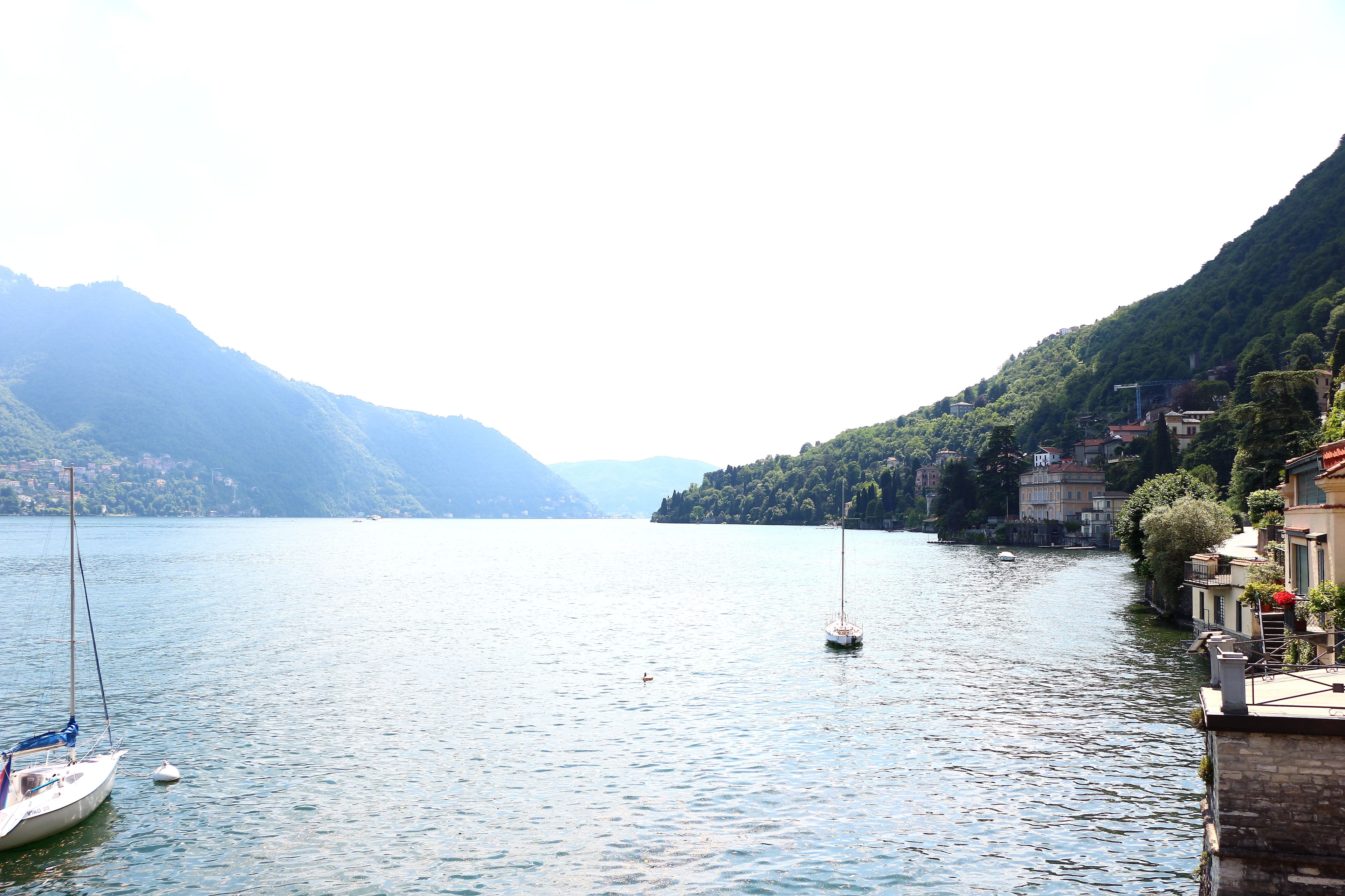 A calm lake with boats, surrounded by mountains and buildings.
