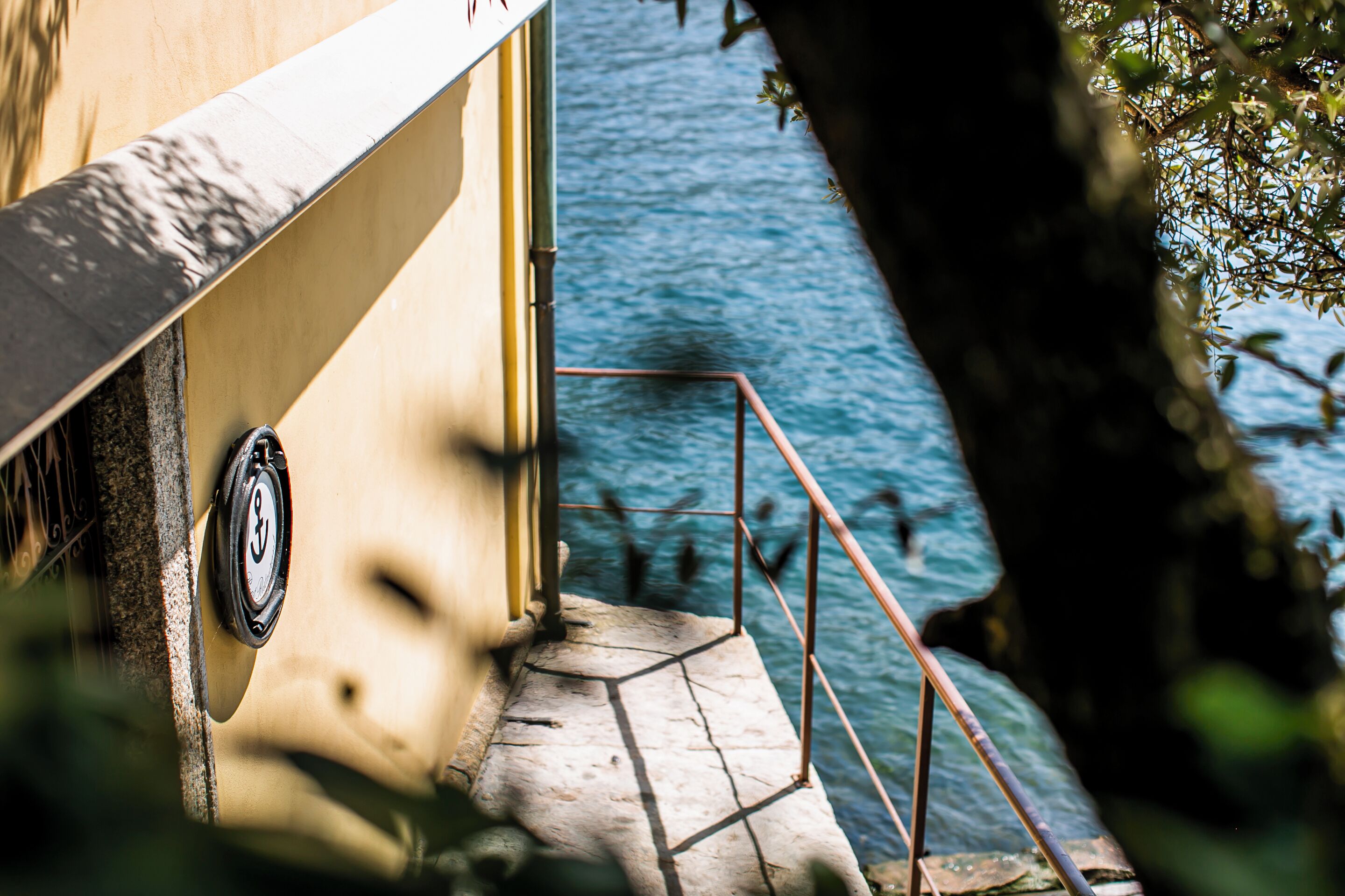 A stone staircase leading to a balcony overlooking a body of water, with a metal railing and a door with a lock.