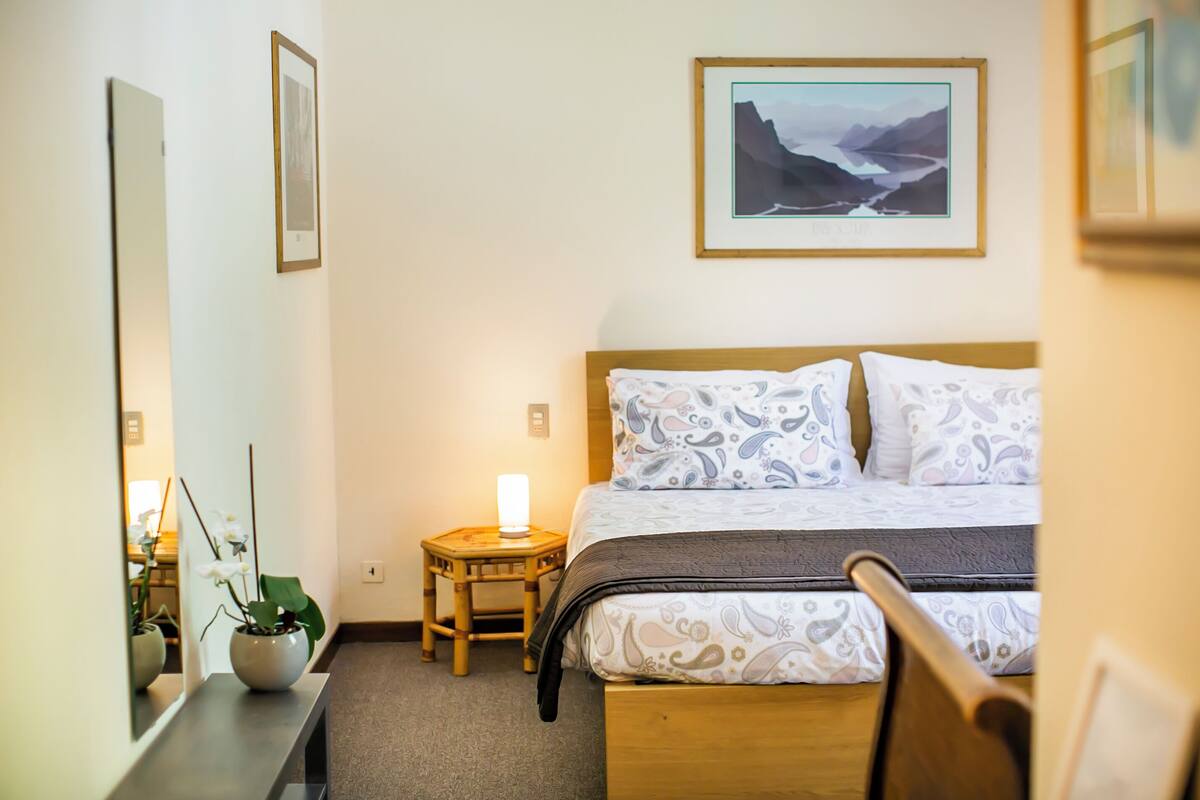 A neatly arranged bedroom with a bed, bedside table, lamp, and a framed picture on the wall.