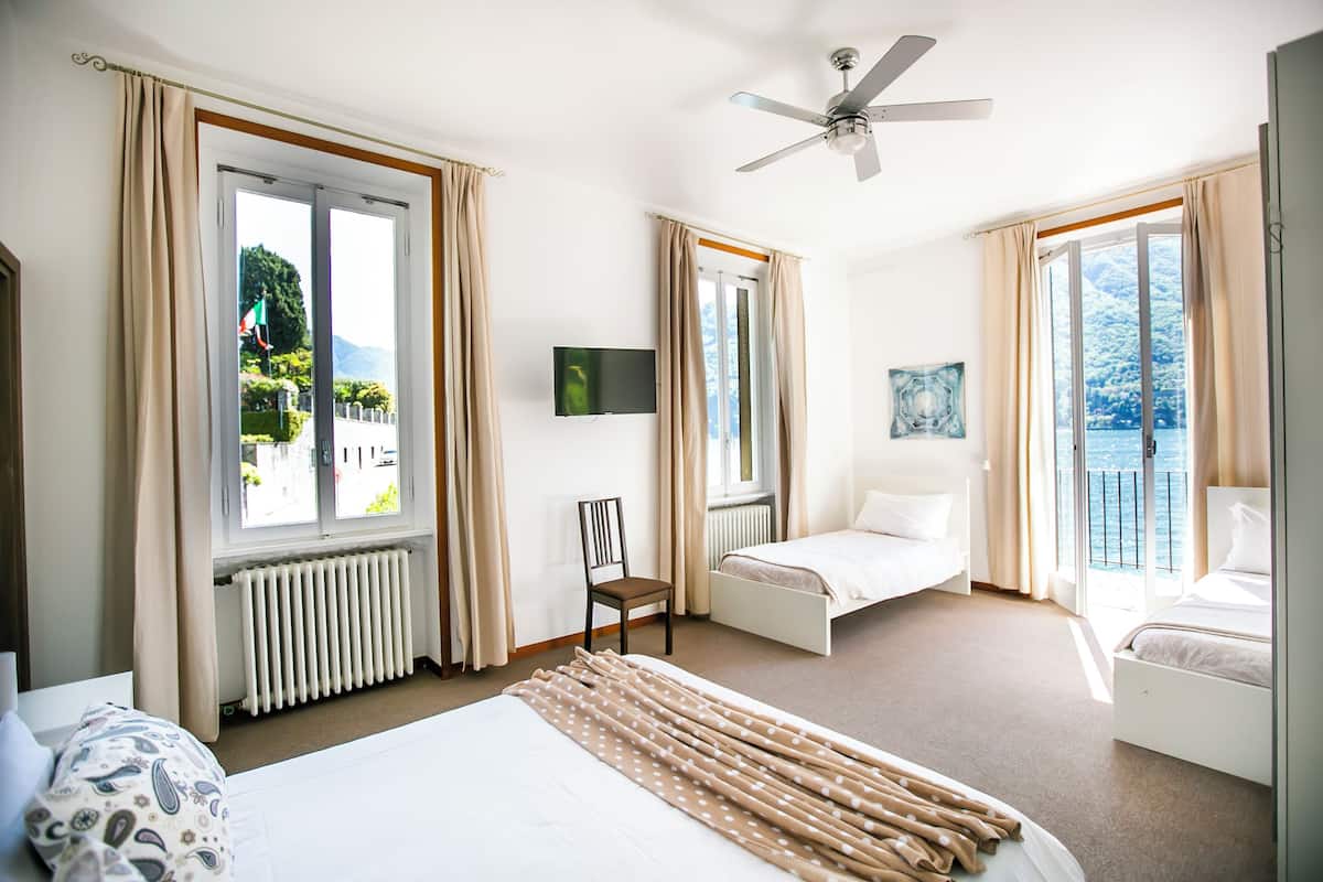 A hotel room with a bed, a chair, a TV, and a balcony with a view of the sea.