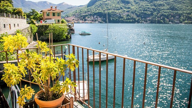 Una vista panorámica de un lago con barcos, una casa y montañas al fondo.