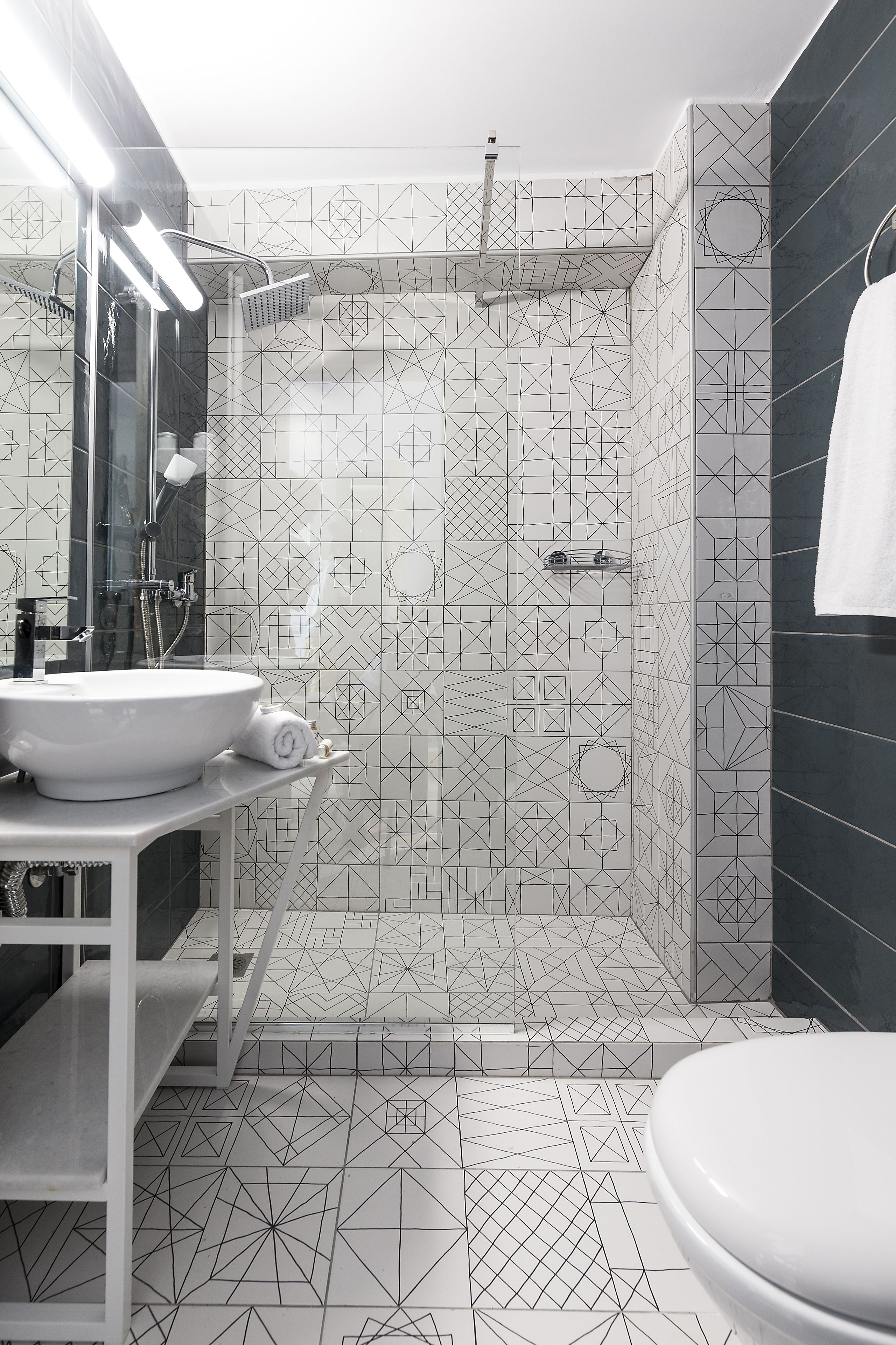 A modern bathroom with a geometric tile pattern, a white sink, and a shower area.
