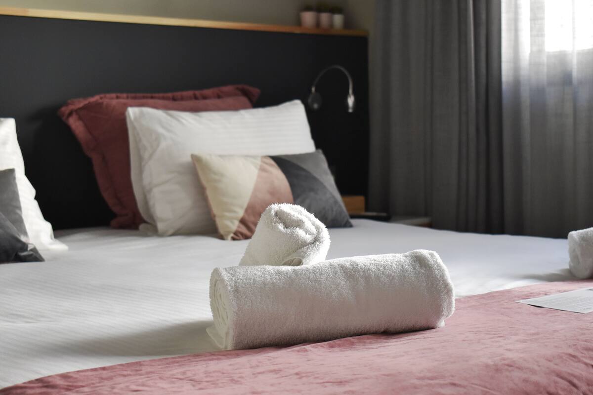 A neatly made bed with a pink blanket and rolled white towels.
