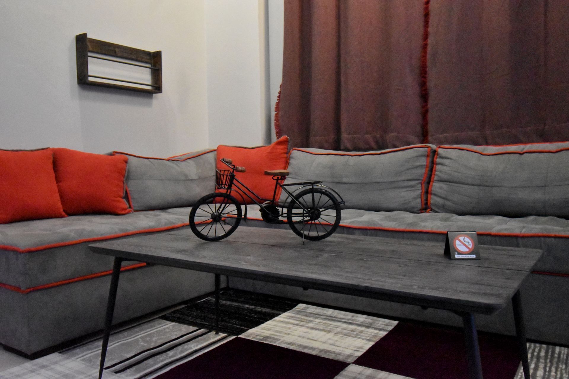 A modern living room with a grey sofa, red cushions, a black bicycle, and a small table.