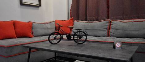 A modern living room with a grey sofa, red cushions, a black bicycle, and a small table.