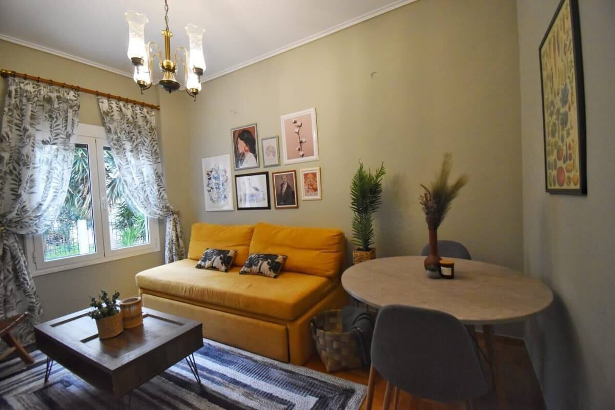 A living room with a yellow sofa, a coffee table, a dining table with chairs, and a chandelier.