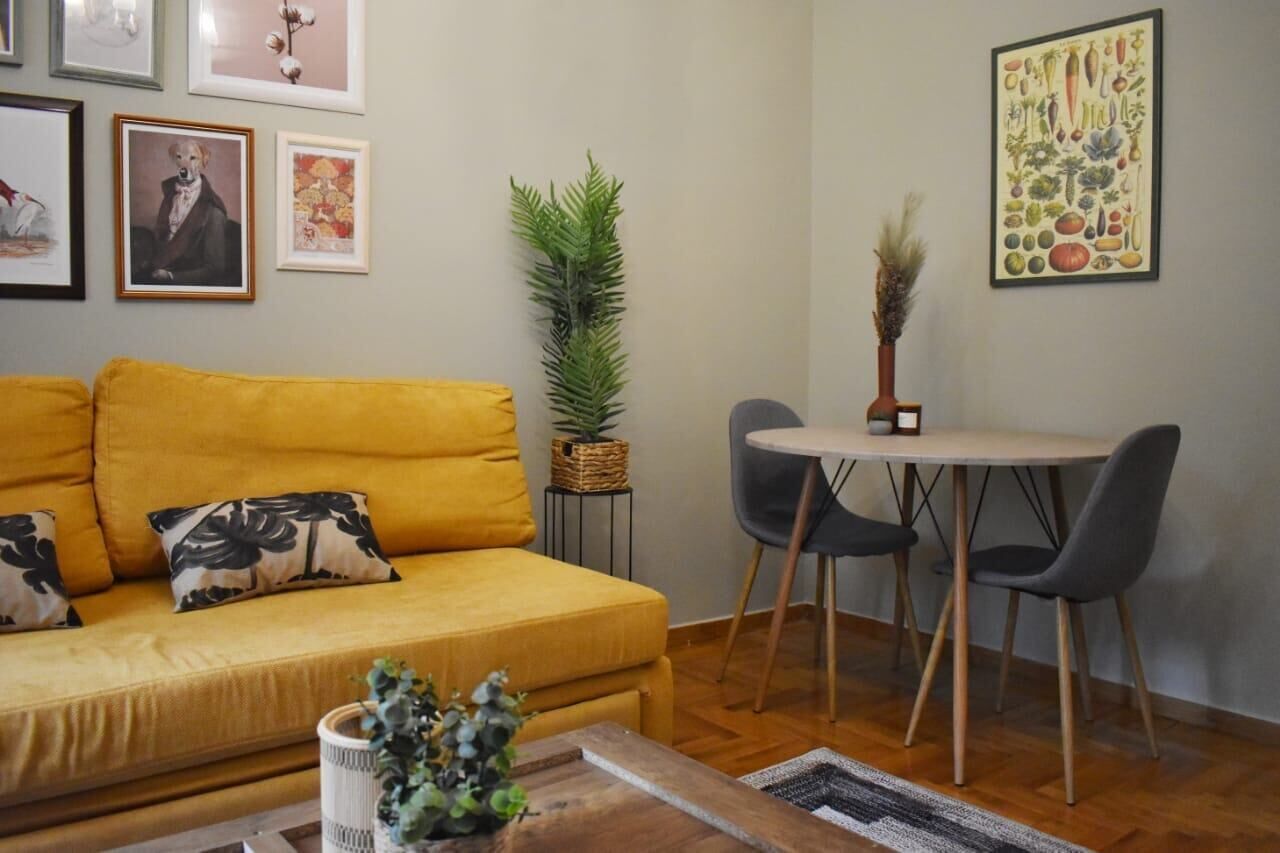 A living room with a yellow sofa, a small round table with two chairs, and framed artwork on the walls.