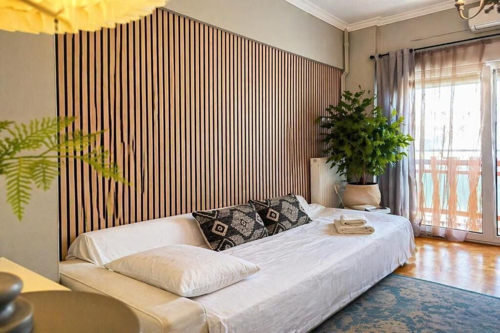 A modern bedroom with a sofa bed, a potted plant, and a view of a balcony.