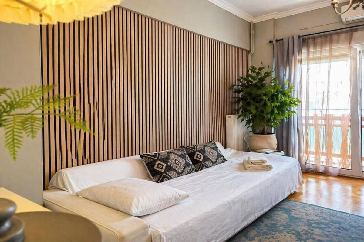 A modern bedroom with a sofa bed, a potted plant, and a view of a balcony.