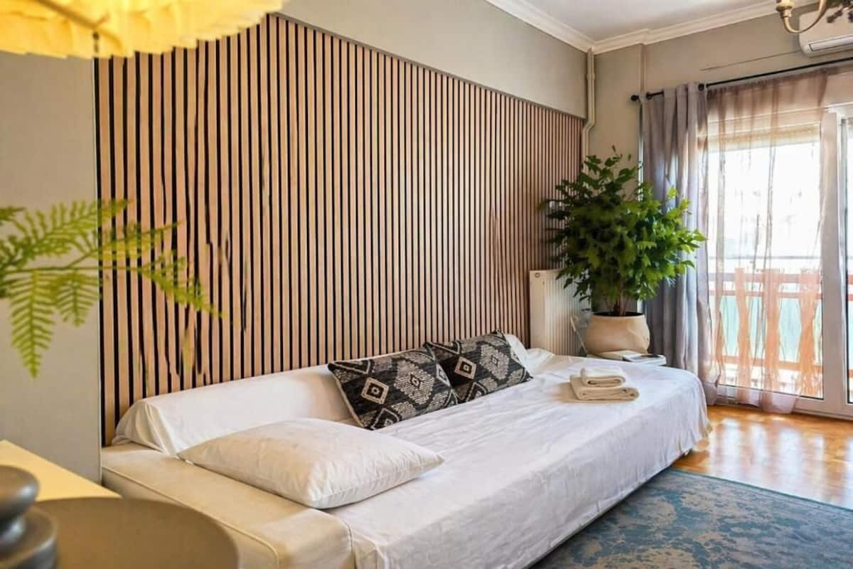 A modern bedroom with a sofa bed, a potted plant, and a view of a balcony.