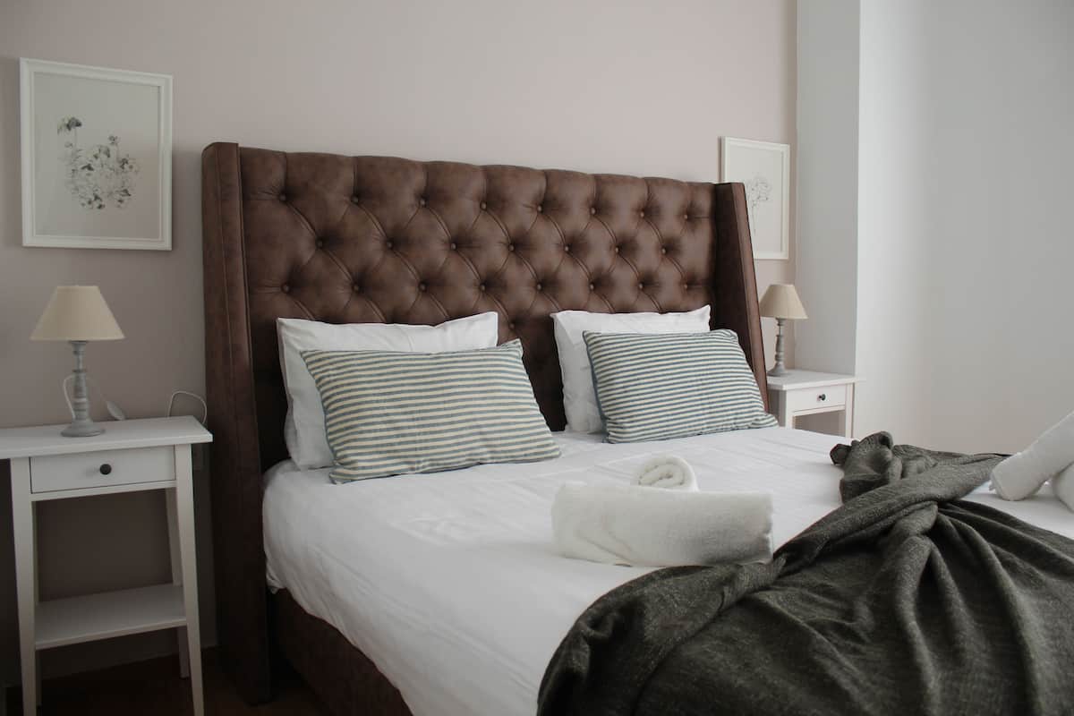 A neatly made bed with a tufted headboard, two bedside tables with lamps, and a framed artwork on the wall.